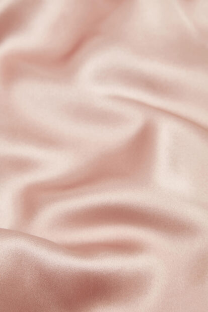 Smooth satin texture in soft pink fabric with elegant folds and gentle light reflections
