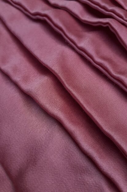 Close up of smooth satin fabric with folds and texture in pink satin