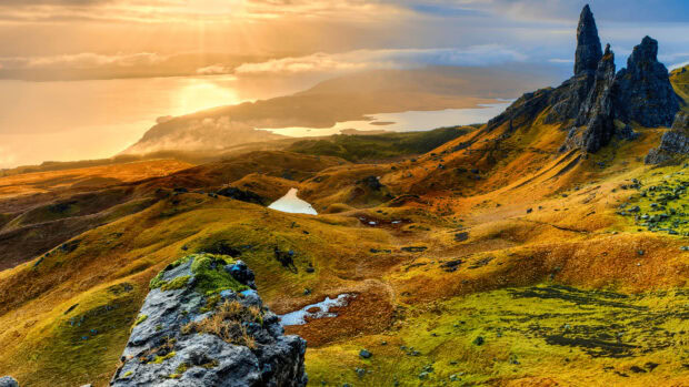 Golden sunlight illuminates the rugged Scotland landscape with towering rock formations and rolling hills