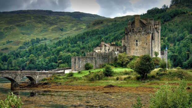 Historic Scotland castle surrounded by lush green hills and a stone bridge over water