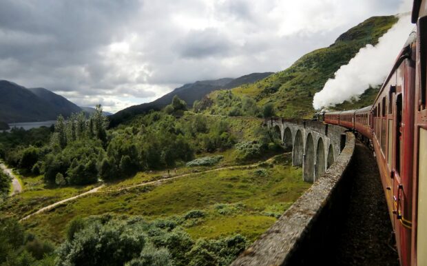 Scenic Scotland landscape with a vintage train crossing a stone viaduct over green hills