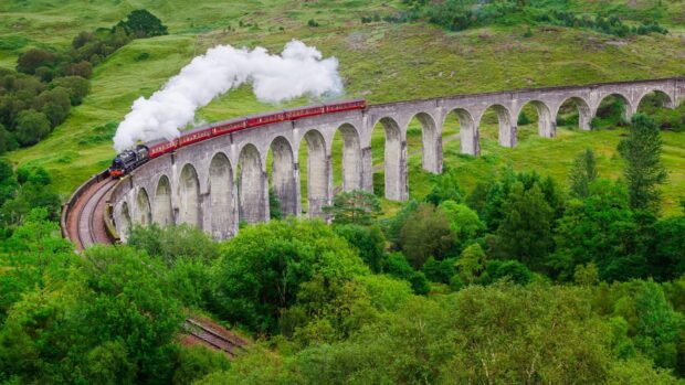 Vintage steam train crossing a historic railway viaduct in Scotland's green landscape