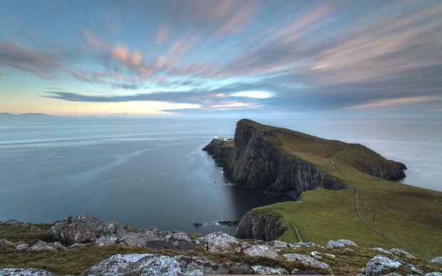 A scenic view of Scotland coastline with cliffs and a lighthouse under a colorful sky