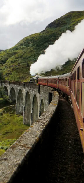 Vintage steam train crossing a stone viaduct in scenic Scotland landscape