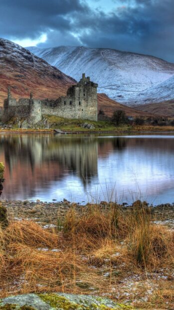 Ancient castle ruins by the lake with Scottish mountains in the background on a cloudy day