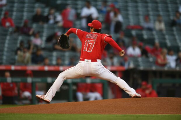 Shohei Ohtani pitching on the mound wearing a red jersey and white pants in a stadium with fans