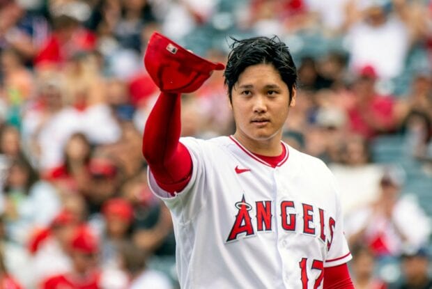 Shohei Ohtani wearing Angels uniform and raising his cap to the crowd in a baseball game