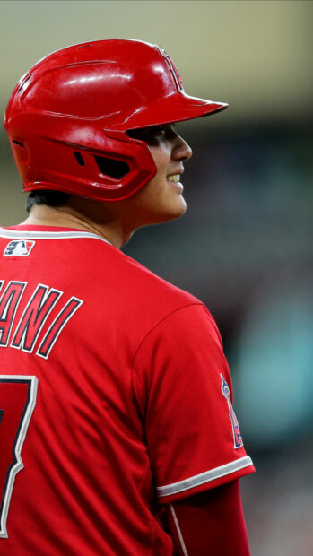 Shohei Ohtani wearing a red baseball helmet and jersey while smiling on the field