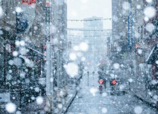 Heavy snowfall covering a city street with buildings and hanging lights during winter