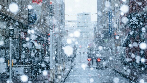 Heavy snowfall covering a city street with buildings and hanging lights during winter