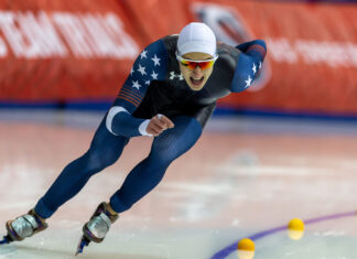 A male athlete in a blue suit racing in a speed skating competition on ice