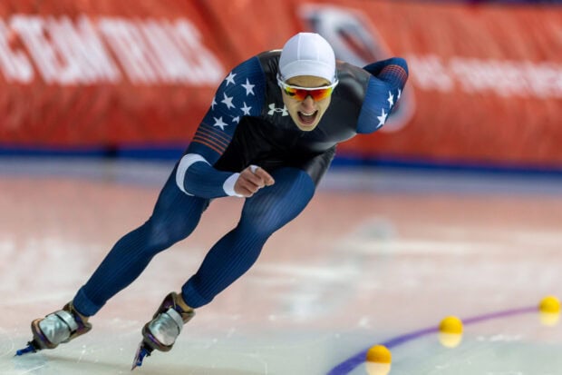 A male athlete in a blue suit racing in a speed skating competition on ice