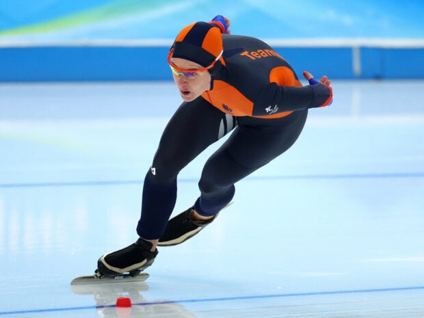 A speed skating athlete wearing an orange and black suit racing on the ice rink