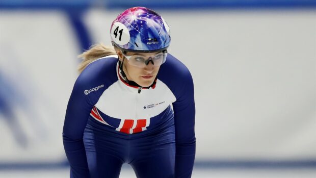Female speed skater in blue and white suit preparing to race on ice rink