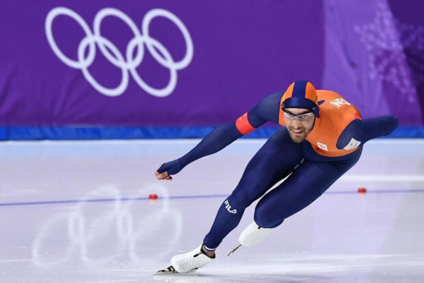 Male speed skater in blue and orange suit competing on ice rink