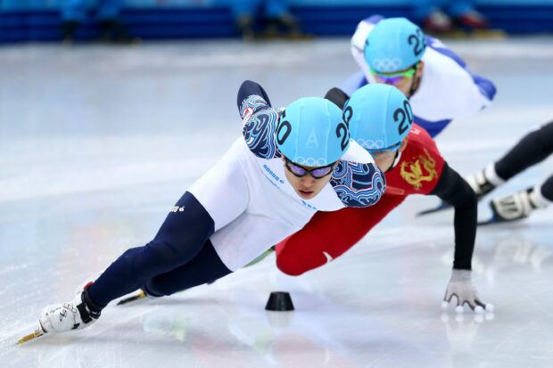 Male speed skater in blue helmet accelerating around the ice in a speed skating race