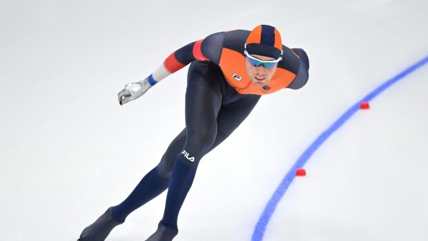 Male speed skater in orange and black suit racing on ice track