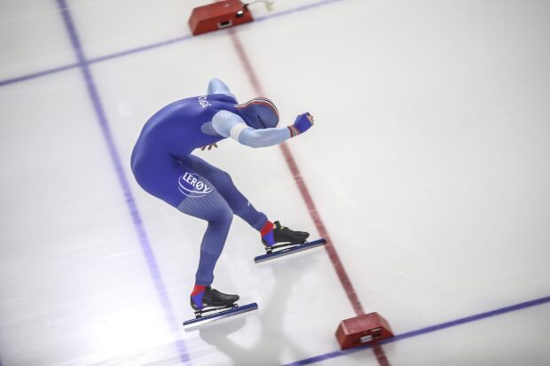 A speed skater in blue suit racing on ice during a speed skating competition