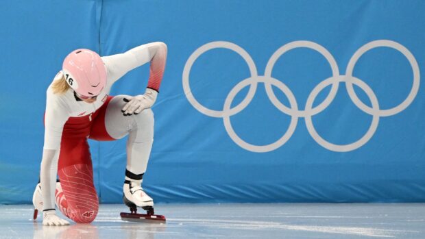 A speed skater in red and white suit preparing on ice during a competition