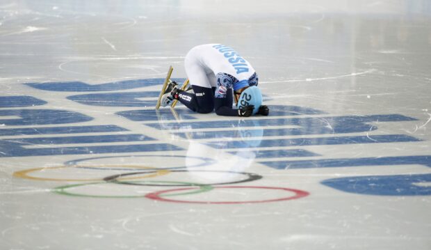 A speed skating athlete from Russia kneeling on the ice after finishing a race