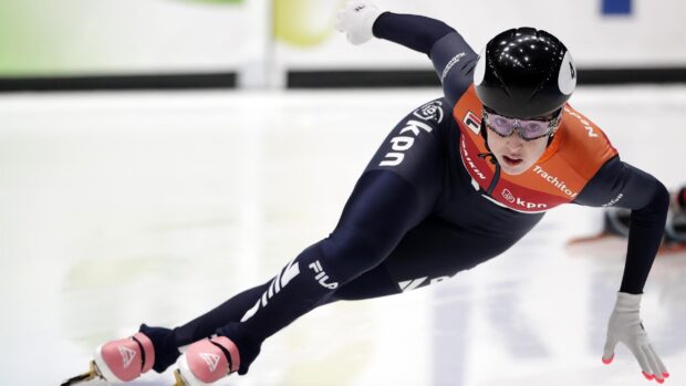A speed skating athlete in a blue and orange suit gliding on ice during a race
