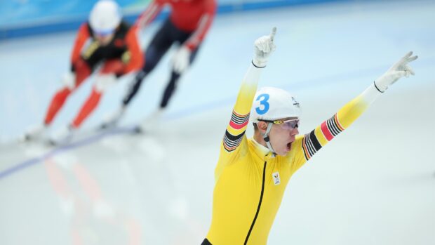 A speed skating athlete in a yellow suit celebrates victory on the ice rink