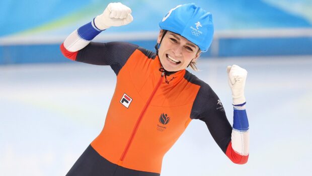 Female speed skater celebrating victory on the ice wearing a blue helmet and orange suit