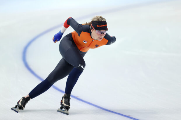 A speed skater in an orange and black suit racing on the ice during competition