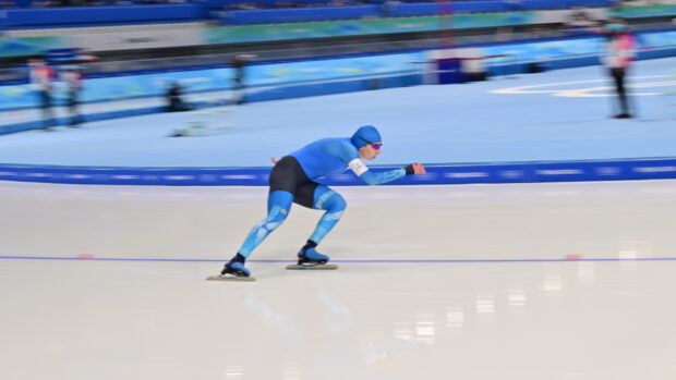 A speed skater wearing blue suit and helmet skating fast on ice rink