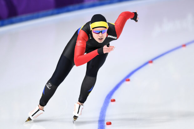 A speed skating athlete in a black and red suit gliding on ice during a race