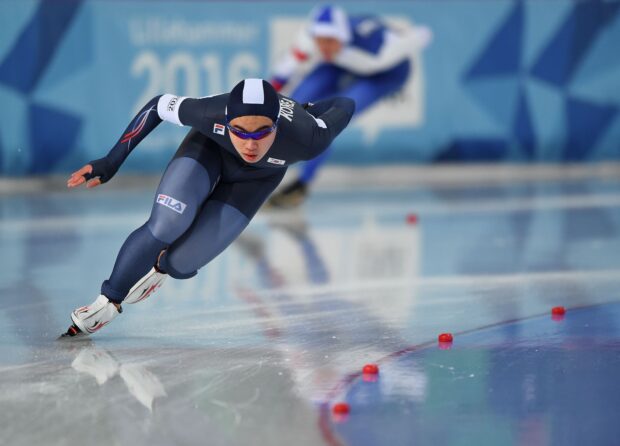 Male speed skater in black suit racing on ice rink during competition