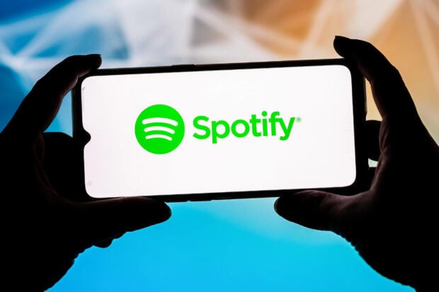 A person holding a phone displaying the Spotify logo in bright green on a white screen
