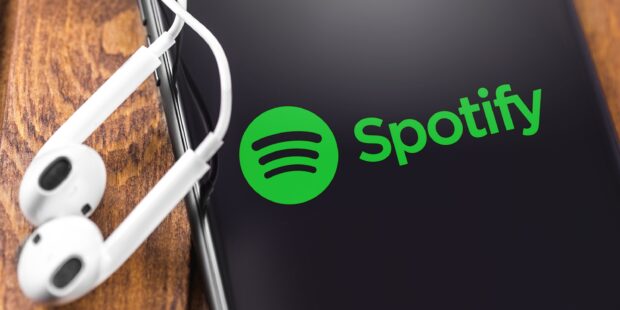 Close up of Spotify logo on a phone screen with white earphones on a wooden surface