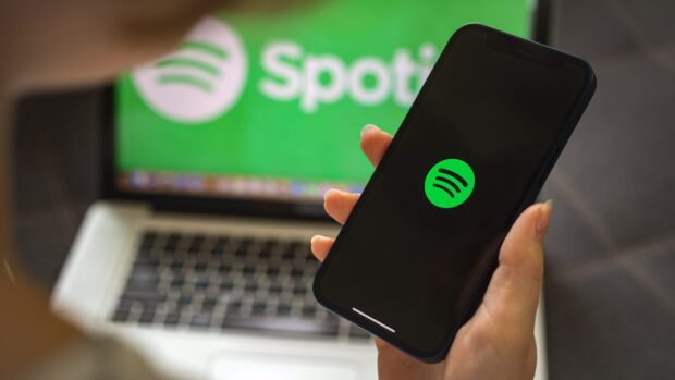 A person holding a phone with Spotify logo displayed on the screen in front of a laptop with Spotify text visible