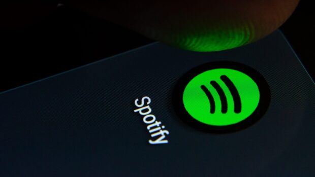 A finger about to tap the Spotify app icon on a mobile screen with Spotify text visible
