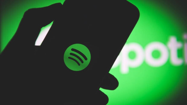 A hand holding a phone showing the Spotify logo on a green screen