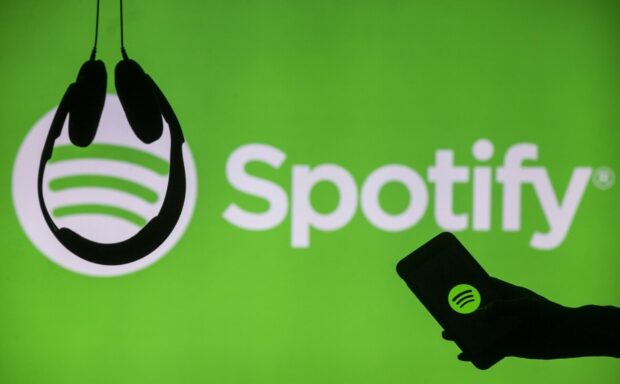 A hand holding a phone with Spotify logo in front of headphones and green Spotify background