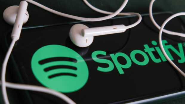 White earphones lying on a phone screen displaying the Spotify logo