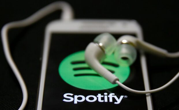 White earphones lying on a phone displaying Spotify logo