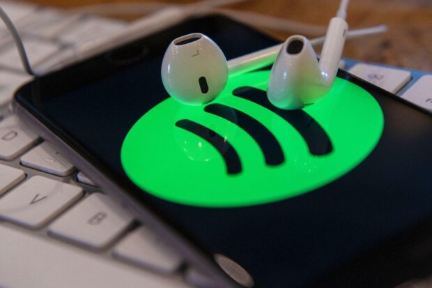 White earphones placed on a phone screen displaying the Spotify logo