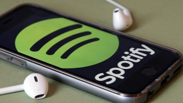 Spotify logo displayed on a phone screen with white earbuds nearby