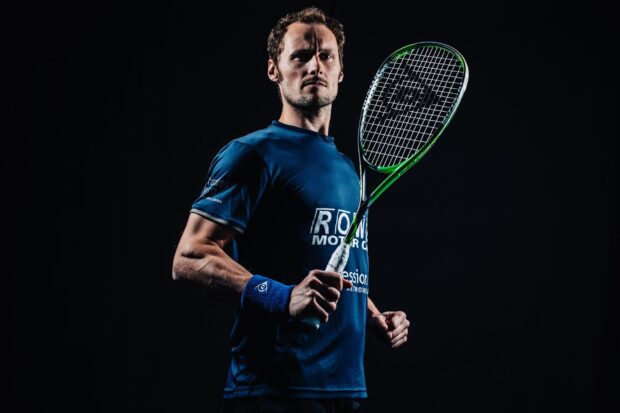 Athletic squash player holding a racket in a ready stance against a dark background