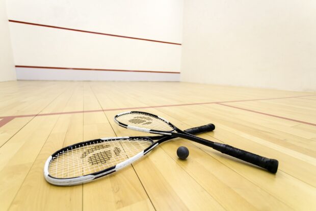 Two squash rackets and a ball on a wooden squash court floor