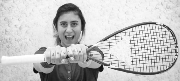 Woman holding squash racket with squash written on her knuckles smiling