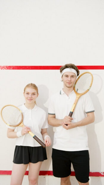 Two young squash players holding wooden rackets in a squash court