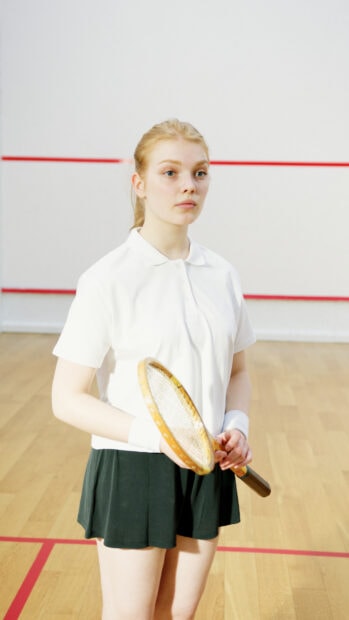 Young woman holding a squash racket standing on the squash court ready to play