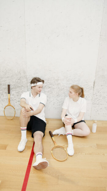 Two squash players sitting on court floor after match conversation with rackets and water bottle nearby