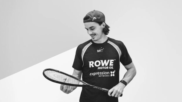 A man holding a squash racket wearing a sports shirt and cap