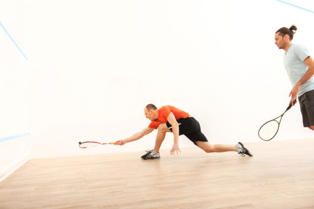 Male squash player lunging forward to hit the ball during a squash sport match