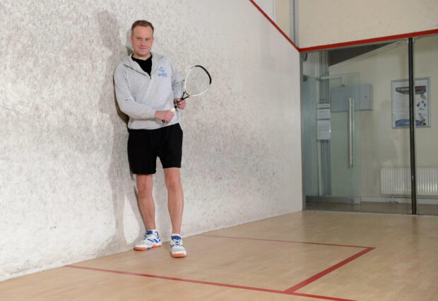 Man holding squash racket standing on court wall playing squash sport